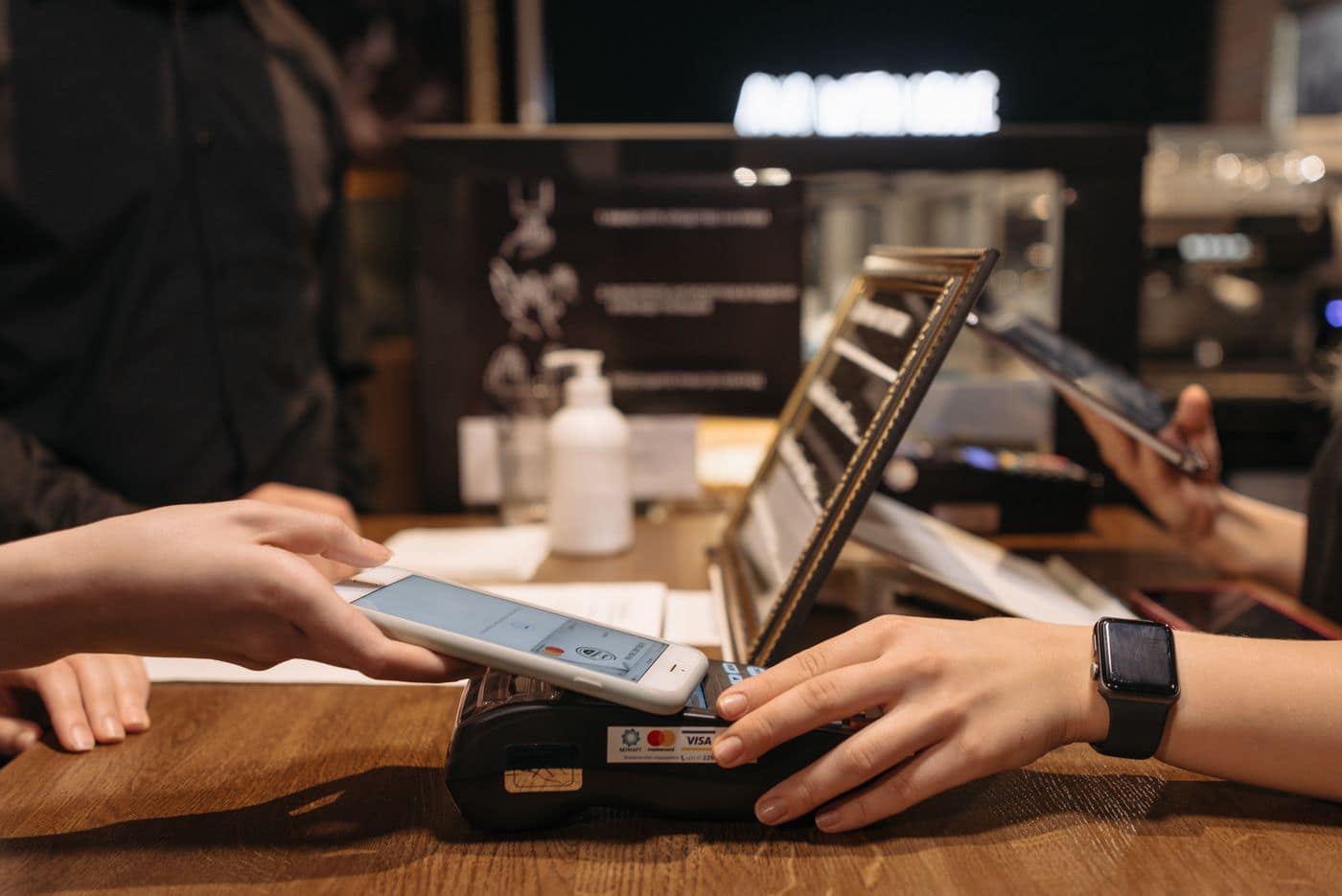 A phone held against a contactless card terminal on a café counter, the payment going through.