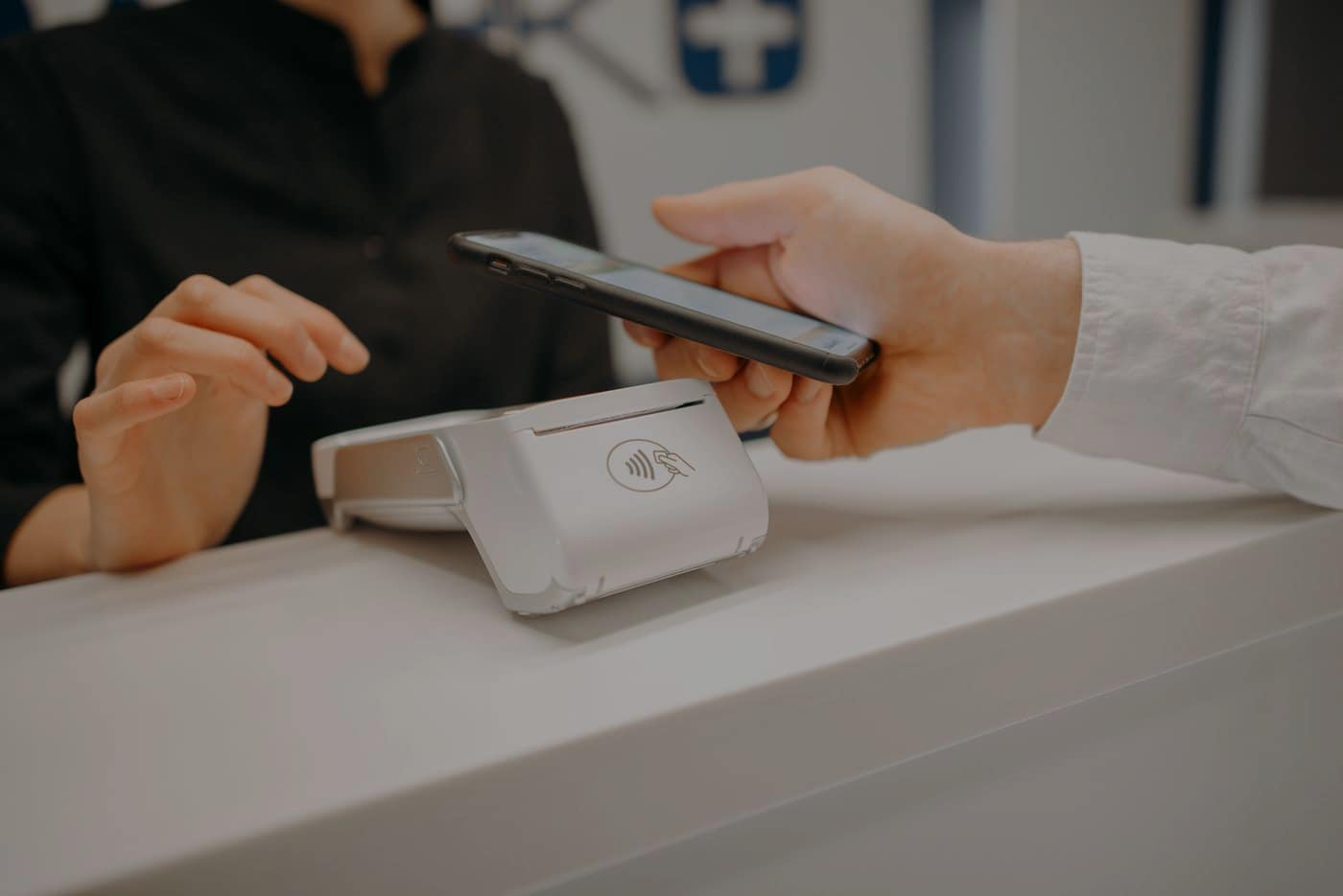 A phone held over the contactless mark on a terminal across a shop counter.