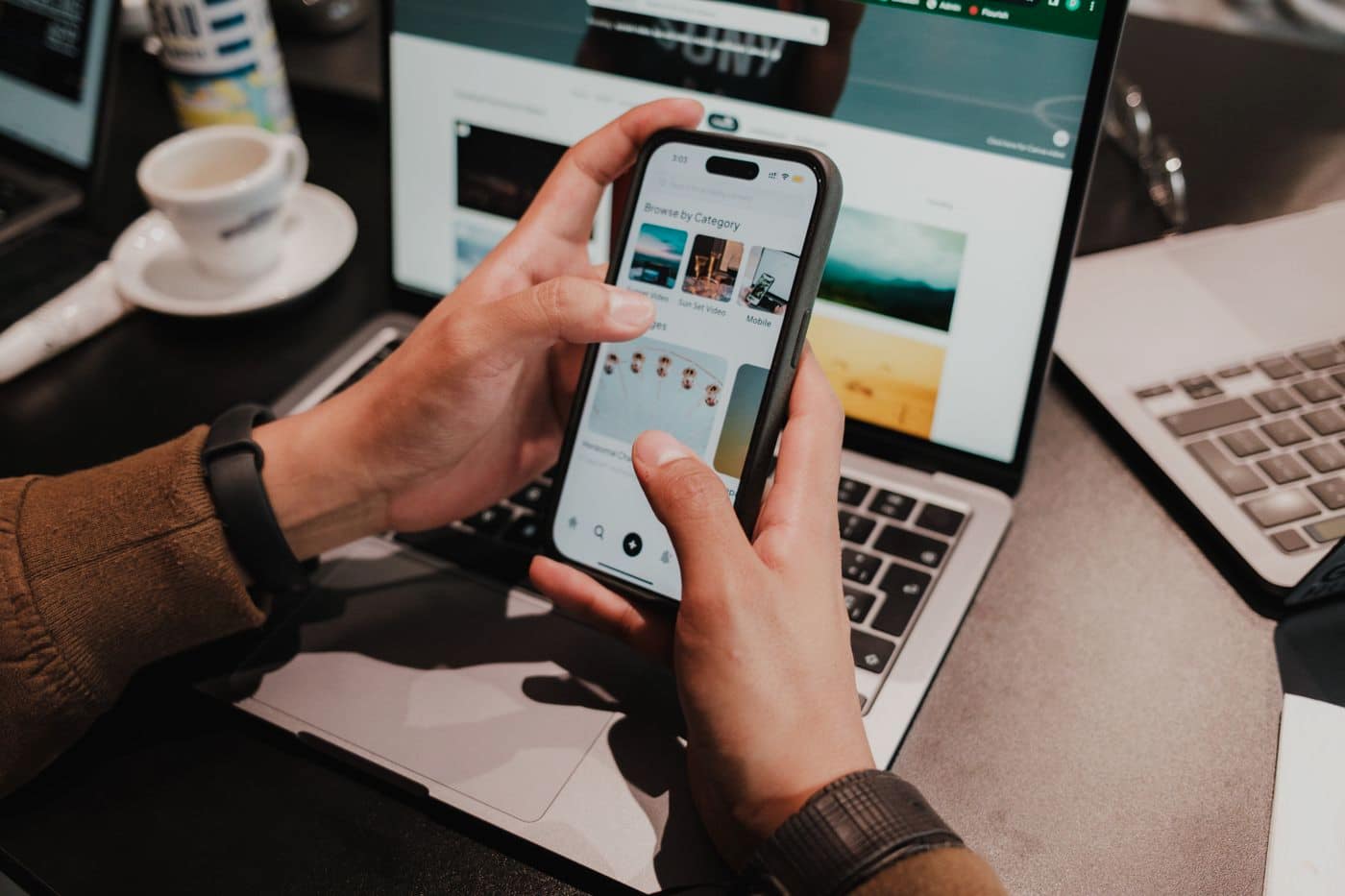 A close view of two hands working a phone over an open laptop.